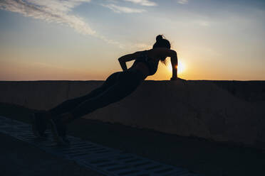 Silhouette einer weiblichen Athletin, die bei Sonnenaufgang an der Promenade Liegestütze macht, in voller Länge - OYF00137