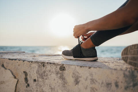 Tiefschnitt einer Sportlerin beim Binden von Schnürsenkeln auf der Promenade, lizenzfreies Stockfoto