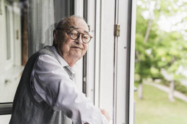 Portrait of smiling senior man standing at open window - UUF20218