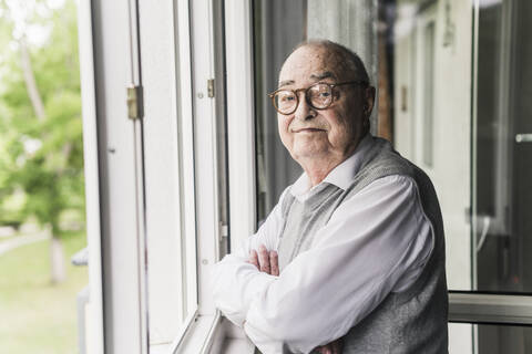 Porträt eines älteren Mannes, der am offenen Fenster steht, lizenzfreies Stockfoto