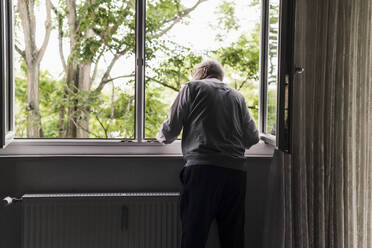 Back view of senior man looking out of window - UUF20221