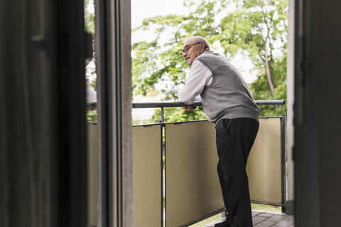 Neugieriger älterer Mann steht auf dem Balkon und beobachtet etwas, lizenzfreies Stockfoto