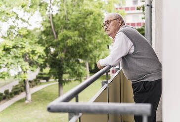 Älterer Mann steht auf einem Balkon und schaut in die Ferne - UUF20227