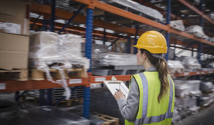 Female factory worker with clipboard checking inventory in warehouse - CAIF26741