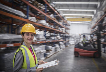 Portrait confident, smiling female worker with clipboard in warehouse - CAIF26745