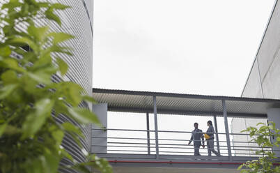 Supervisors walking on elevated walkway between factory buildings - CAIF26750