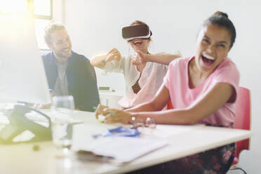 Lachende Computerprogrammierer, die eine Virtual-Reality-Simulatorbrille im Büro testen - CAIF26774