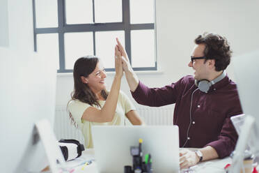 Computer programmers high-fiving at laptop in office - CAIF26776