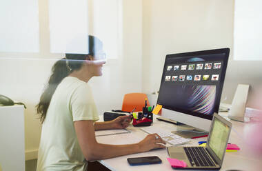 Weibliche Designerin betrachtet Bildminiaturen am Computer im Büro - CAIF26815