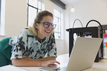 Lächelnde Designerin bei der Arbeit am Laptop neben dem 3D-Drucker im Büro - CAIF26885