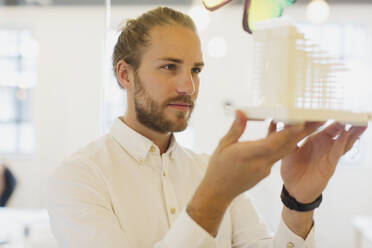 Focused, curious male architect examining model in office - CAIF26886