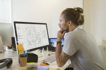 Fokussierter männlicher Architekt, der einen digitalen Bauplan am Computer betrachtet - CAIF26940