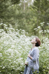 Schwangere Frau mit Händen auf dem Bauch entspannt inmitten von Blumen im Park - EYAF01052