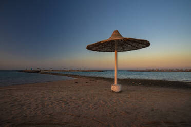 Ägypten, Hurghada, Strohschirm am Sandstrand der Sahl Hasheesh Bucht in der Abenddämmerung - TAMF02205