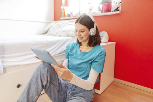 Portrait of smiling teenage girl with headphones and digital tablet learning at home - STDF00215