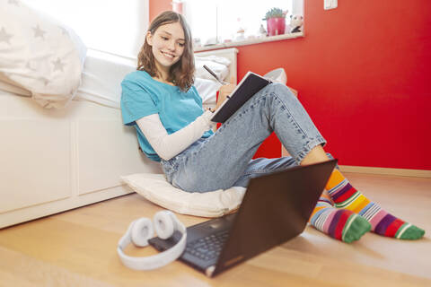 Portrait of smiling teenage girl learning with laptop at home stock photo