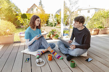 Teenage couple sitting on terrace learning together with laptop and digital tablet - STDF00219