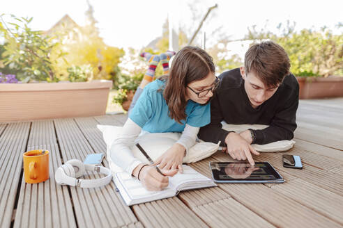 Teenager-Paar auf der Terrasse liegend und mit digitalem Tablet lernend - STDF00221