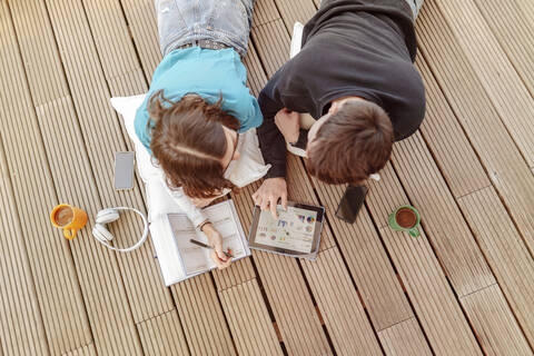 Teenager-Paar auf der Terrasse liegend und mit digitalem Tablet lernend, lizenzfreies Stockfoto