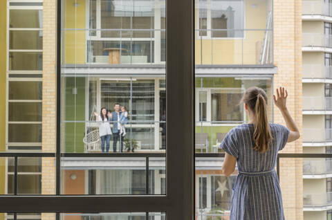 Rückansicht einer Frau, die auf einem Balkon steht und ihren Nachbarn zuwinkt, lizenzfreies Stockfoto