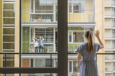 Back view of woman standing on balcony waving to her neighbours - AHSF02449