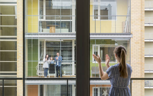 Back view of woman on balcony clapping hands and looking to her neighbours - AHSF02452