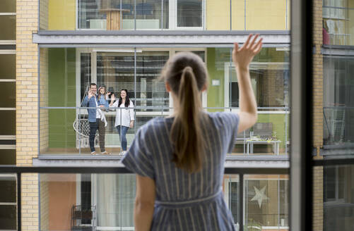 Rückansicht einer Frau, die auf einem Balkon steht und ihren Nachbarn zuwinkt - AHSF02455
