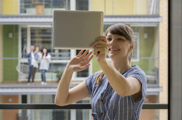 Portrait of smiling young woman using digital tablet for video chat with her neighbours - AHSF02456