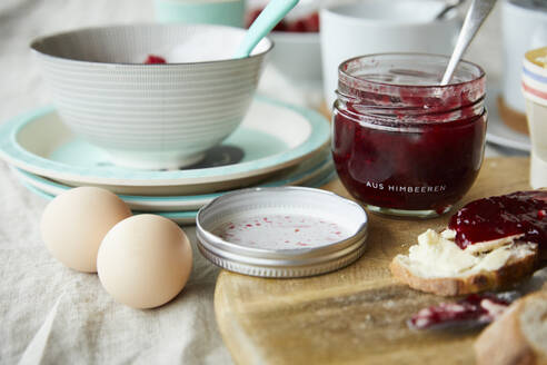 Ein Glas Himbeermarmelade, Brot mit Marmelade und zwei Eier auf dem Frühstückstisch - FSF01066