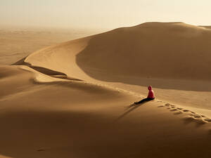 Frau sitzt allein auf dem Kamm einer Düne in der Wüste, Walvis Bay, Namibia - VEGF02082