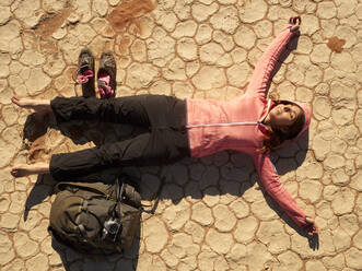 Barfüßige Frau und ihr Rucksack liegen auf dem rissigen Boden der Trockenpfanne in Deadvlei, Namibia. - VEGF02087