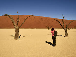 Frau fotografiert einen der von Dünen umgebenen Bäume im Deadvlei, Namibia. - VEGF02092