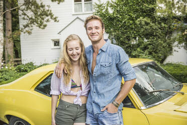 Portrait of young couple standing in front of yellow vintage car in summer - SDAHF00794