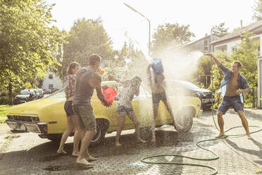 Eine Gruppe von Freunden wäscht einen gelben Oldtimer im Sommer und hat Spaß dabei - SDAHF00800