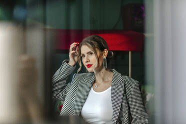 Porträt einer schönen Frau mit rotem Lippenstift, die aus dem Fenster schaut - OGF00328
