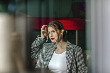 Portrait of beautiful woman with red lipstick looking out of window - OGF00328