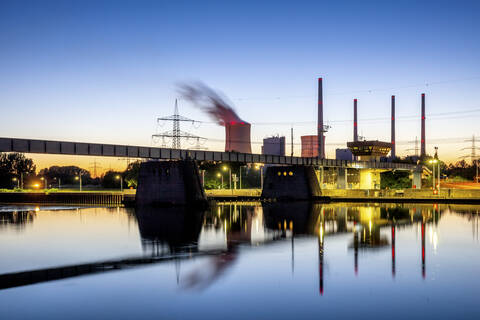 Deutschland, Hessen, Großkrotzenburg, Kraftwerk Großkrotzenburg mit Spiegelung im Main in der Abenddämmerung, lizenzfreies Stockfoto