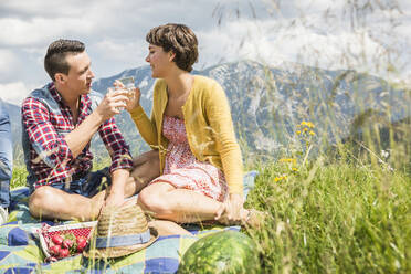 Couple having a picnic on a meadow in the mountains clinking glasses, Achenkirch, Austria - SDAHF00815