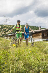 Mountainbike schiebendes Paar auf einer Bergwiese, Achenkirch, Österreich - SDAHF00827