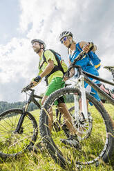 Mountainbike schiebendes Paar auf einer Bergwiese, Achenkirch, Österreich - SDAHF00828