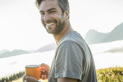 Portrait of a happy man holding coffee mug in the mountains at dawn, Achenkirch, Austria - SDAHF00887