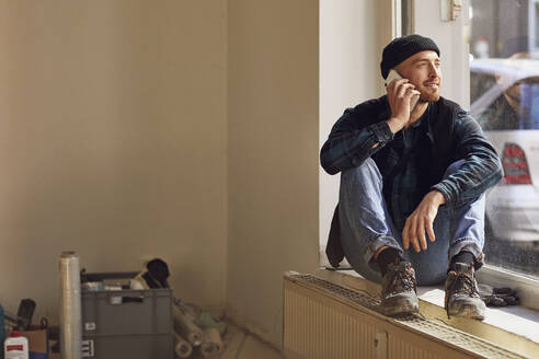 Man refurbishing shop location, sitting on windowsill, talking on the phone - MCF00794