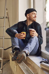 Man refurbishing shop location, sitting on windowsill, drinking coffee - MCF00806