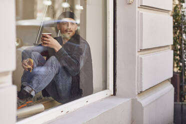 Man refurbishing shop location, sitting on windowsill, drinking coffee - MCF00807