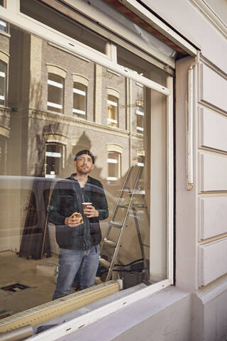 Mann renoviert Ladenlokal, trinkt Kaffee, schaut aus dem Fenster, lizenzfreies Stockfoto