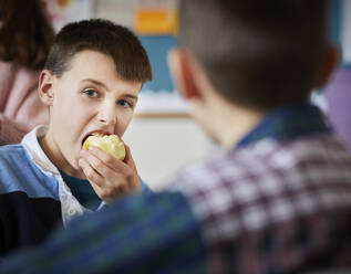 Junge in einem Klassenzimmer in der Pause, der einen Apfel isst - PWF00056