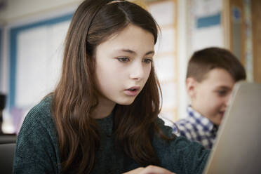 Mädchen und Junge in einem Klassenzimmer während einer Unterrichtsstunde über Laptops - PWF00078