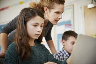 Mädchen und Junge in einem Klassenzimmer während einer Unterrichtsstunde über Laptops mit einem Lehrer - PWF00079