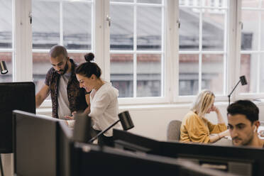 Business professionals discussing while colleagues working at creative office - MASF17926