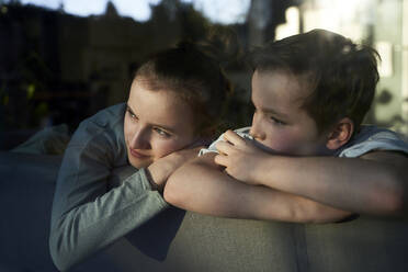 Bruder und Schwester auf der Couch zu Hause und schauen aus dem Fenster - AUF00364